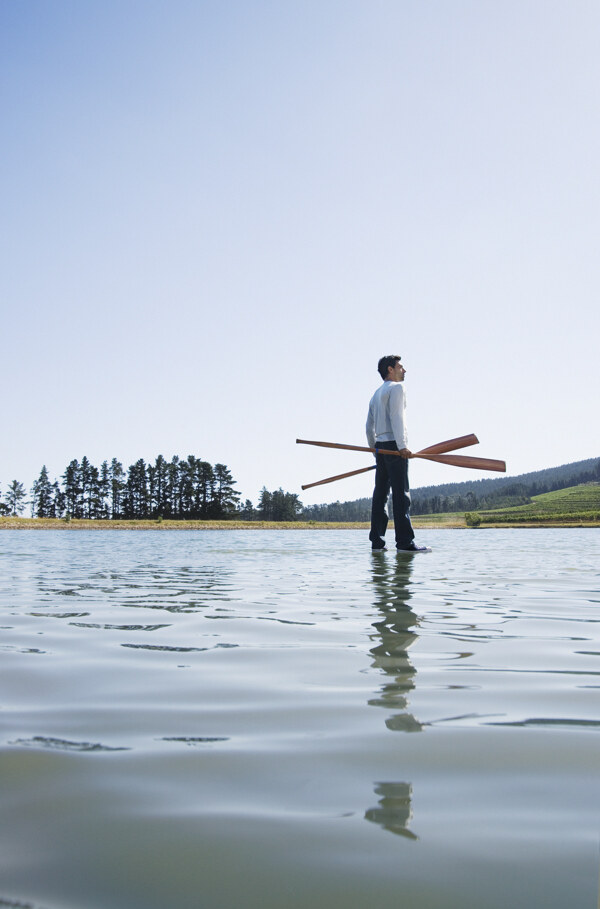 手拿双桨站立在水面上的男人图片