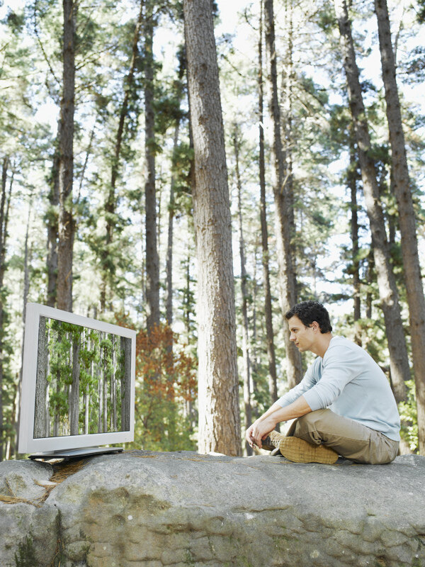 坐在巨石上看电视的男人图片