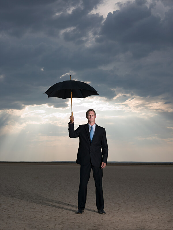 阴天打伞站在沙漠里的外国商业男人图片