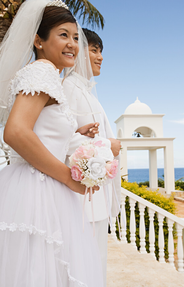 穿着婚纱礼服手捧鲜花站在海边远望的男女图片图片