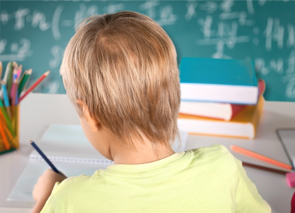 一个金发小男孩正在写满公式的黑板和堆叠的书籍中学习