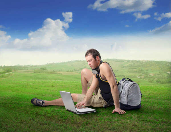 草原上玩电脑的时尚青年男性图片